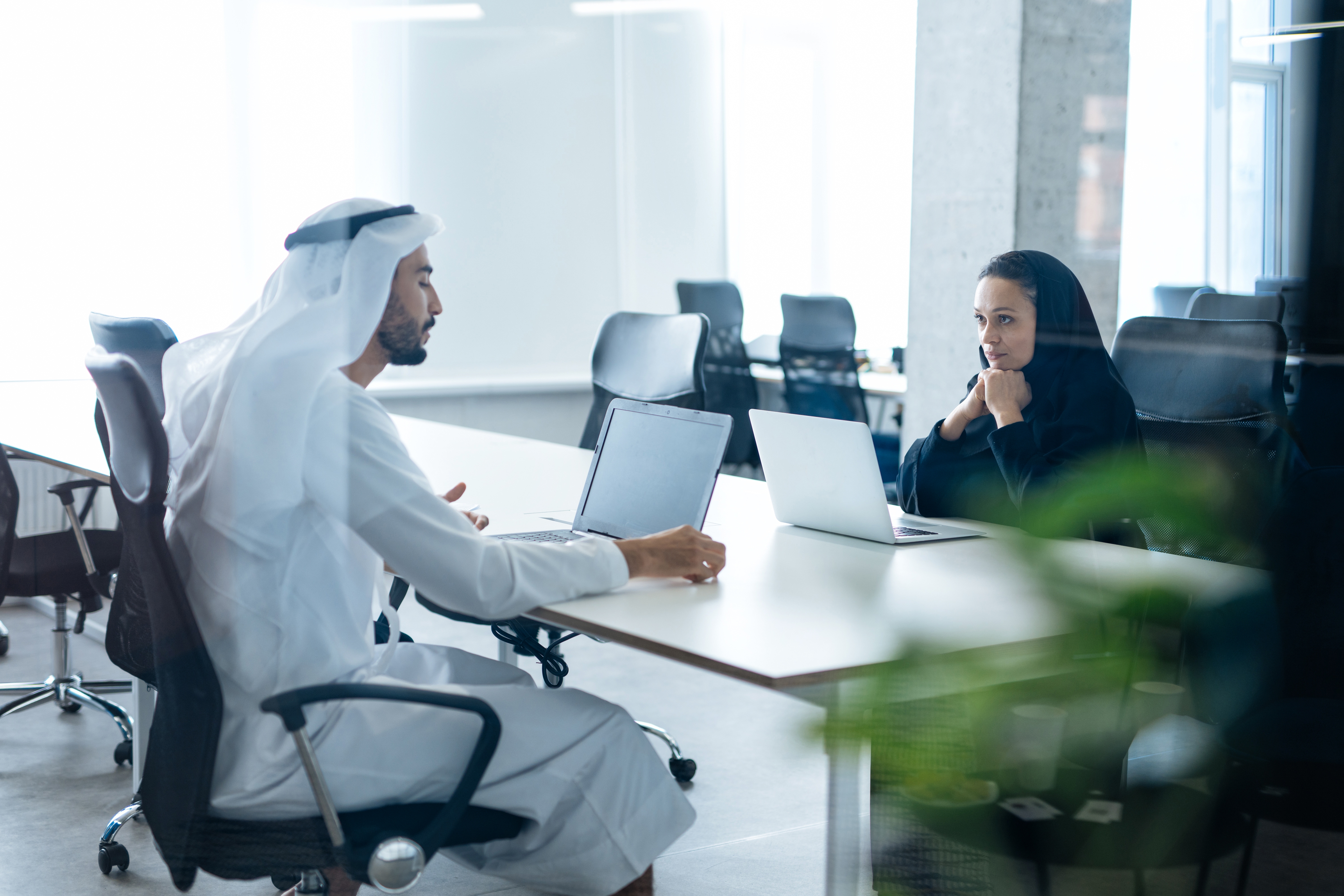 Arab man and woman sitting opposite each other in office in the office with laptops in front of them