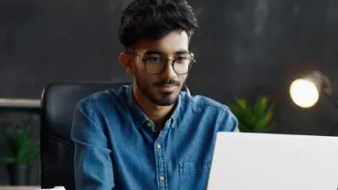 Man with glasses working on a laptop in a modern office.