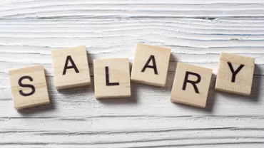 Wooden Scrabble tiles spelling 'SALARY' on a white wooden surface.