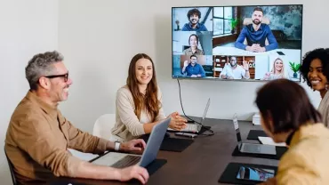 Happy office employees in the office in a conference room havvng a video call on the big screen