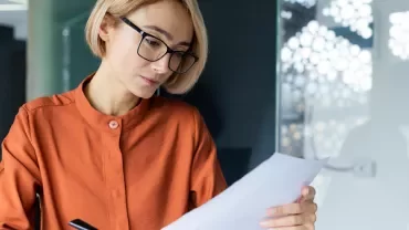Woman with blonde hair and glasses reading a piece of paper