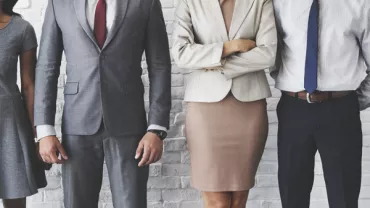 Business professionals in formal attire standing against a brick wall.