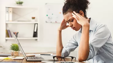 Woman sitting at a desk, looking stressed with her hands on her temples.