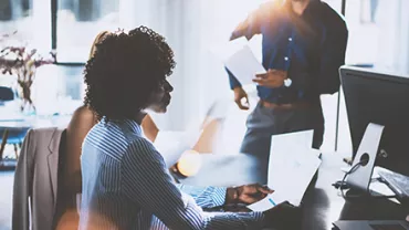 People in an office setting, discussing documents.