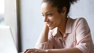 Smiling woman working on a laptop near a window.