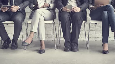 Row of business professionals seated, holding mobile devices and laptops.