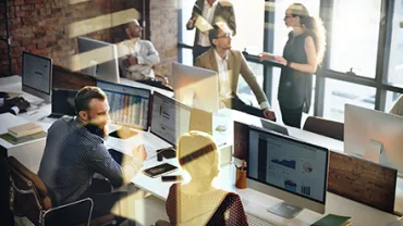 Group of colleagues discussing work in a modern office with computers.