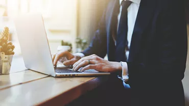 Businessperson typing on a laptop at a sunlit desk.