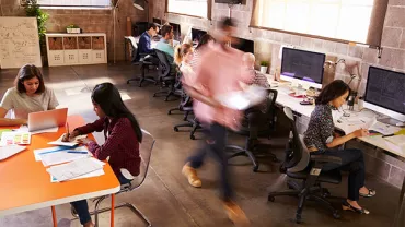 Open office space with people working on computers and papers.