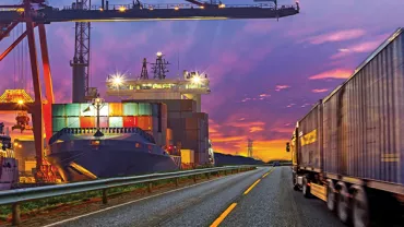 Cargo ship and truck at port during vibrant sunset, showcasing logistics.