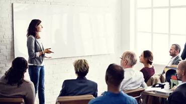 Person giving a presentation to a group in a bright room.