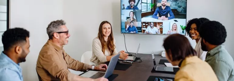 Happy office employees in the office in a conference room havvng a video call on the big screen